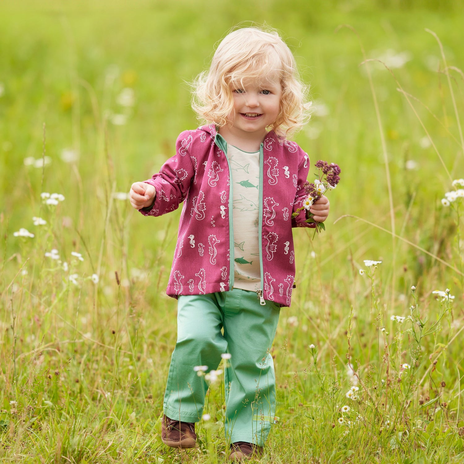 Kind mit wasserabweisender Jacke in Pink auf Wiese